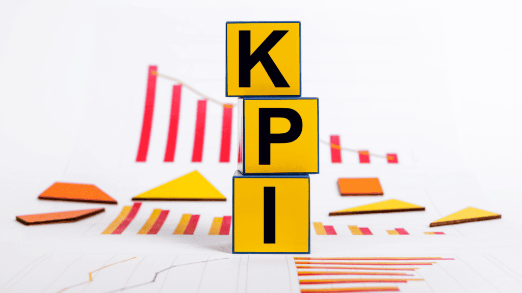 Stack of three yellow blocks with letters "k", "p", and "i" in black, arranged vertically on a table with colorful charts and geometric figures related to Social Media Marketing Strategies for Hospitals in the background.
