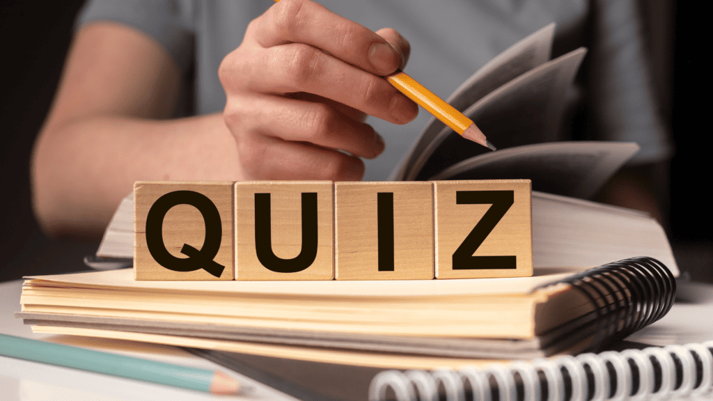 A person holds a pencil over a notebook, with wooden blocks in the foreground spelling "quiz" while brainstorming social media marketing strategies for clothing brands. The setting suggests a study or quiz preparation environment.