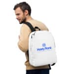A man viewed from the side, wearing a beige jacket and HR Urban Voyager Backpack, smiles over his shoulder. The white backpack displays a blue logo for "hastyrank," described as a job placement and resume company.