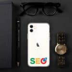 A white smartphone with an "SEO Clear Case for iPhone®" logo on its back, accompanied by a black notebook, pen, glasses, and a gold wristwatch, all neatly arranged on a dark surface.