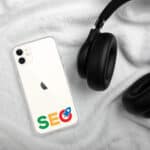 A smartphone with a "SEO Clear Case for iPhone®" lies on a soft white blanket, flanked by a black over-ear headphone. the phone displays colorful seo letters in a search engine style on its back cover.