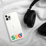 A smartphone with a "SEO Clear Case for iPhone®" label and search engine logos on its case lies between black headphones on a fluffy white surface.