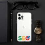 Flat lay of a work desk featuring an SEO Clear Case for iPhone®, a gold watch, black glasses, a notebook, and a pencil on a dark background.