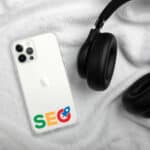 A smartphone with SEO Clear Case for iPhone®-related app icons on the back lies on a white fluffy fabric, next to a pair of black over-ear headphones. the setting suggests a focus on digital marketing and audio technology.