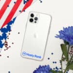 A transparent HR CrystalShield iPhone® Case with a blue hasty rank logo on a white iphone. the phone is surrounded by a folded american flag, red confetti, and blue flowers on a white background.
