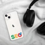 A white smartphone with an SEO Clear Case for iPhone® graphic and Google's logo on the back, next to a pair of black over-ear headphones, all placed on a soft, white, fluffy surface.