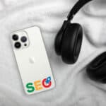 An SEO Clear Case for iPhone with "seo" text and a magnifying glass icon on the back lies on a white fluffy fabric, partially underneath a pair of black over-ear headphones.