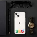 A flat lay composition includes a black notebook, a pen, sunglasses, a gold watch, and a smartphone with a SEO Clear Case for iPhone® on a dark background.