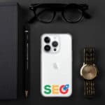 Flat lay of a modern workspace featuring a white SEO Clear Case for iPhone®, a gold wristwatch, a black notebook, a pencil, and black sunglasses, all arranged on a dark background.