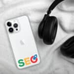 A white smartphone with the "SEO Clear Case for iPhone®" in colorful letters on its back lies on a plush white blanket, partially beneath black over-ear headphones, suggesting a focus on digital marketing and technology.