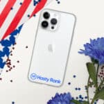 An HR CrystalShield iPhone® Case with a hasty rank logo on the back, surrounded by the u.s. flag, blue flowers, and red star confetti on a white surface.