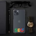 A flat lay of a black surface with items: a notebook, sunglasses, a mechanical pencil, an SEO Clear Case for iPhone®, and a gold wristwatch.