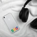 An SEO Clear Case for iPhone, showing the apple logo, on a white fuzzy blanket next to a pair of black headphones. The phone displays colorful letters forming the word "sec" on a white background.