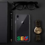 Flat lay of a black iPhone with "SEO Clear Case for iPhone®" text overlay, a gold wristwatch, black sunglasses, a pencil, and notebook, all arranged on a dark surface.