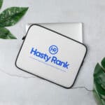 A HR TechGuard Laptop Sleeve with a blue logo reading "hasty rank" lies on a marble surface next to a closed laptop and green leaves, symbolizing a digital marketing company.