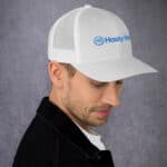A side profile of a caucasian man wearing a white HR SunStride Cap with a blue "hasty ram" logo. he is dressed in a dark jacket over a white shirt, against a textured gray background.