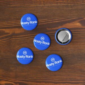 Four blue HR Expressions Pin Sets with the "hasty rank" logo are scattered on a wooden surface, one badge has a pin visible, arranged around a central badge.