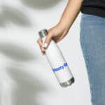 A person in jeans holding a white HR Elite Hydration Flask with "hasty pd" in blue letters. the background is light with shadows of leaves, suggesting a sunny outdoor setting.