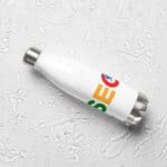 A white reusable SEO Stainless Steel Water Bottle with colorful abstract designs, lying on a flat surface with water droplets scattered around it, reflecting a sense of hydration and eco-friendliness.