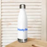 A HR Elite Hydration Flask with a silver cap and base, labeled "hasty ram" in blue text, is placed on a wooden table against a white wooden backdrop.