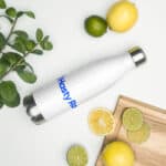 A stainless steel water bottle with "HR Elite Hydration Flask" logo lies on a white surface next to fresh lemons, limes, and mint leaves with a wooden cutting board.
