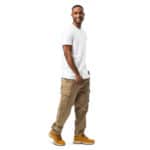 A smiling young man wearing an HR PrimeStyle Tee, beige cargo pants, and yellow boots stands in a side profile pose, looking at the camera against a white background.