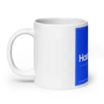A white ceramic mug with a glossy finish featuring a large blue rectangle label with the text "hashtag" in white, followed by the text "a full-stack developer" in smaller font. the HR Cheerful Brew Mug is shown against a plain white background.